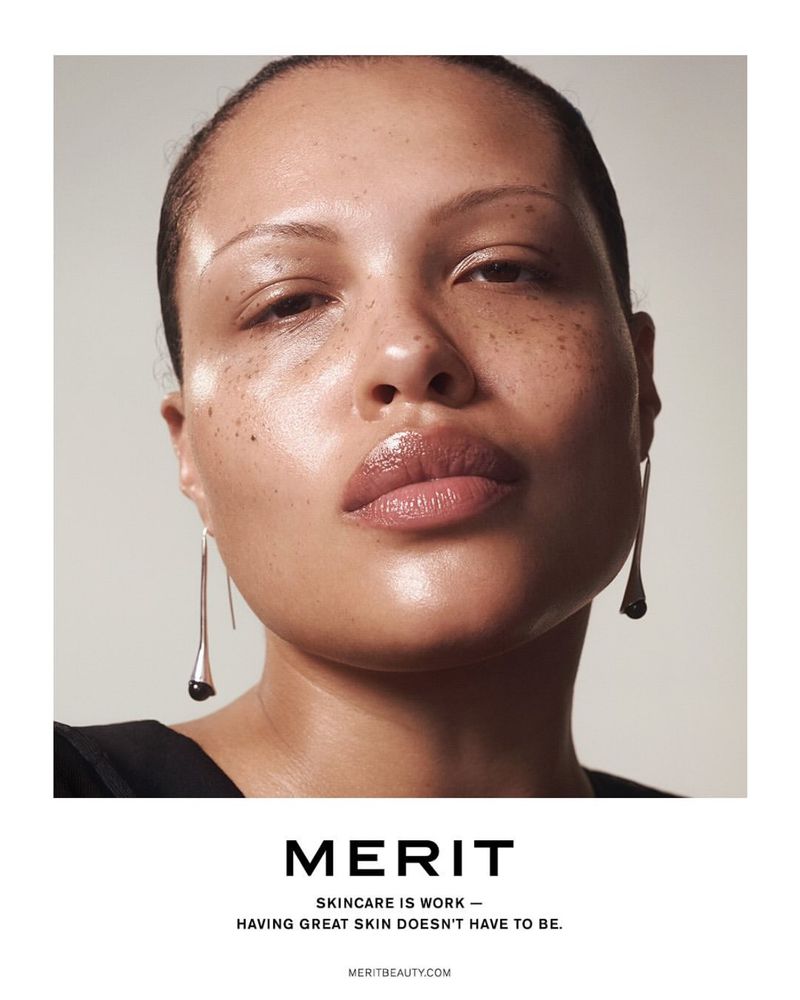 Close-up portrait of a light-skinned adult female with glossy lips and teardrop earrings against a neutral backdrop, beauty advertisement.