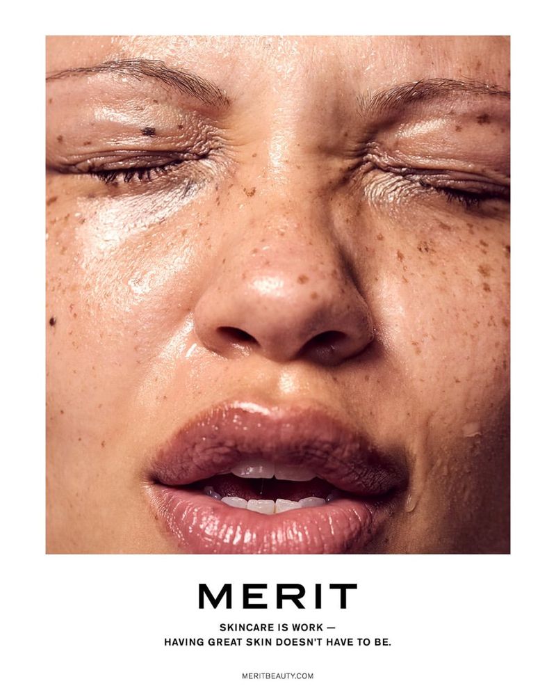 Close-up of a woman's face with eyes closed, featuring shiny, freckled skin. The skincare product is advertised with the brand name Merit.