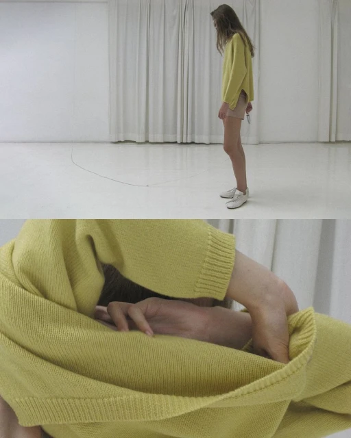 Adult female in a yellow sweater stands in a minimalist studio, captured in medium shot showcasing fashion and simplicity.