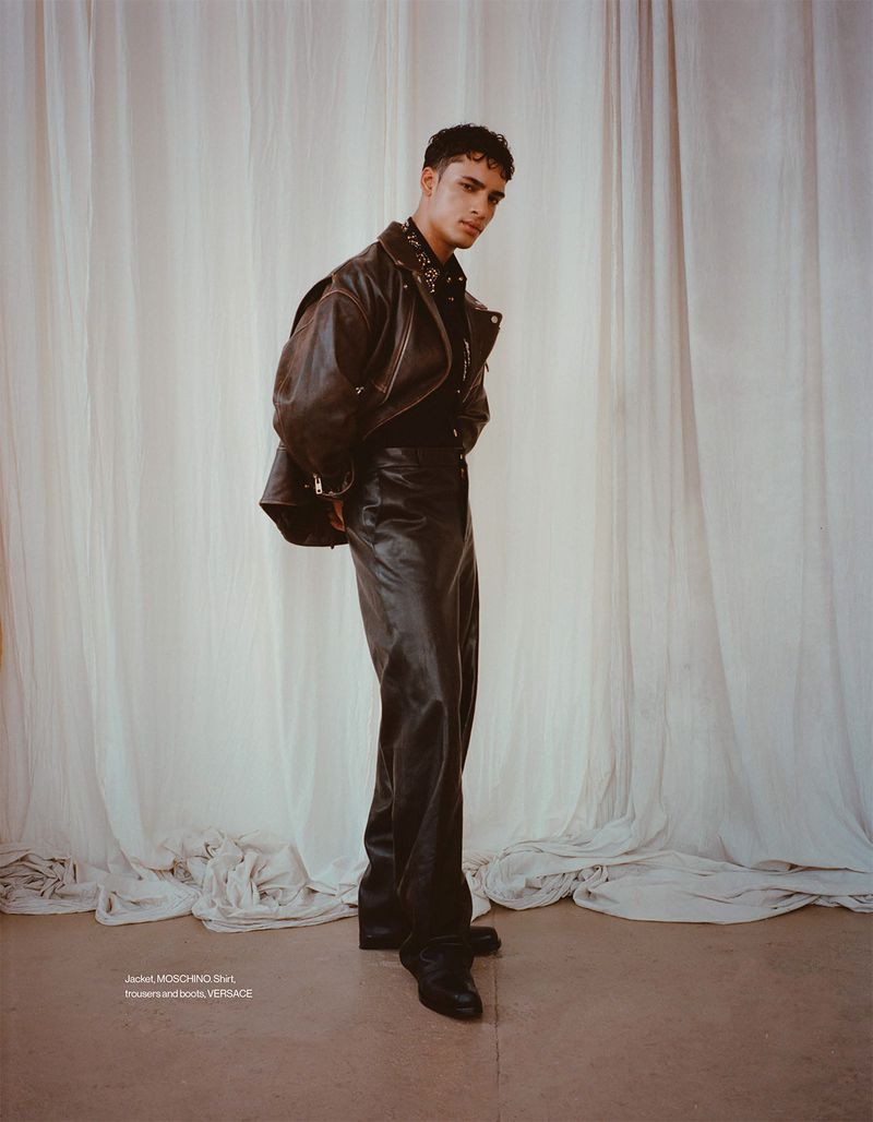 Model Mase Somanlall wearing a brown leather jacket and dark leather trousers in front of draped off-white curtains.