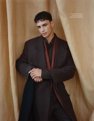 Male model in a dark brown coat and dark shirt posing against draped textured hessian fabric background for Esquire Singapore.