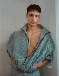 Model Mase Somanlall wearing an unzipped patterned track jacket against a neutral textured wall.