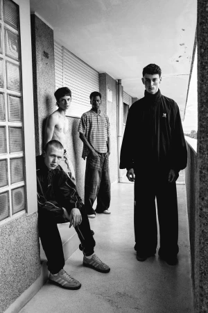 Four young men stand in a hallway, showcasing casual fashion with athletic wear in a black and white photograph with natural lighting.