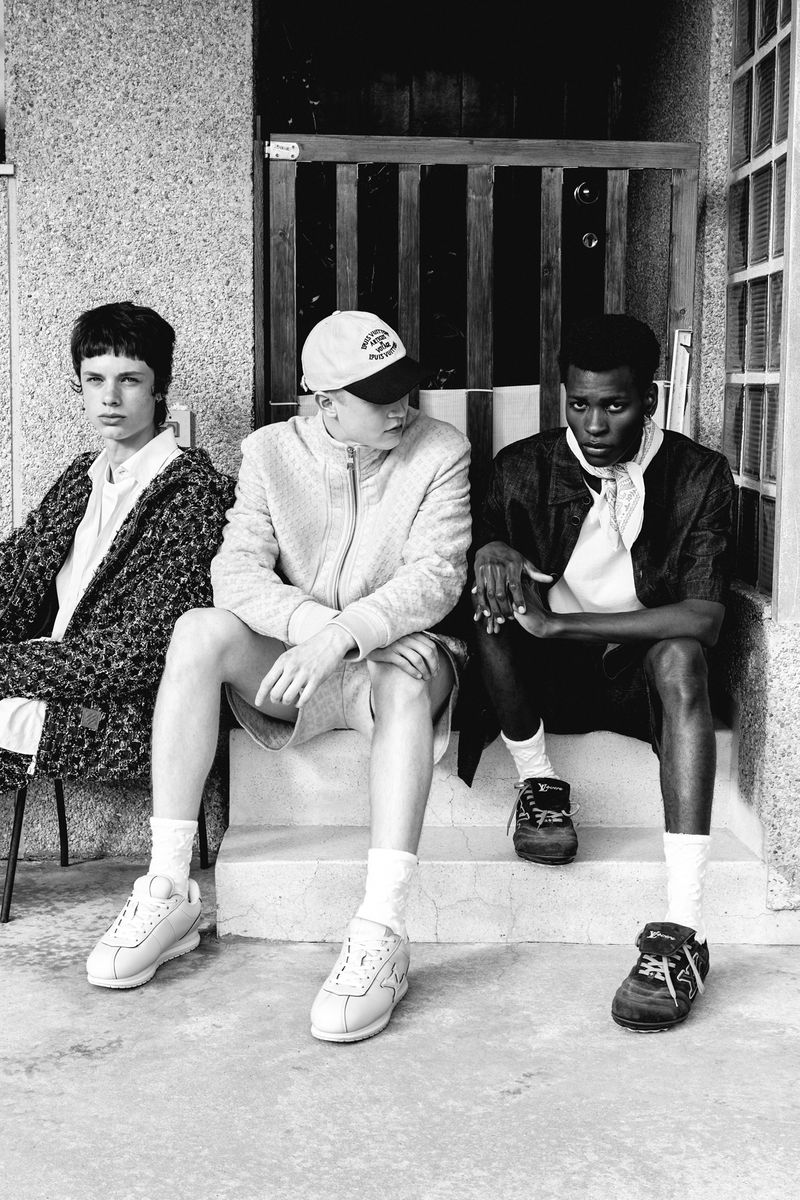 Black and white photograph of three young adult friends in casual fashion sitting outside on steps, showcasing friendship and modern style.