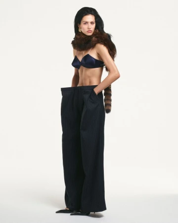 Fashion shot of a woman in a blue bra, oversized pinstripe pants and a fur stole, posing in a photo studio against a white background.