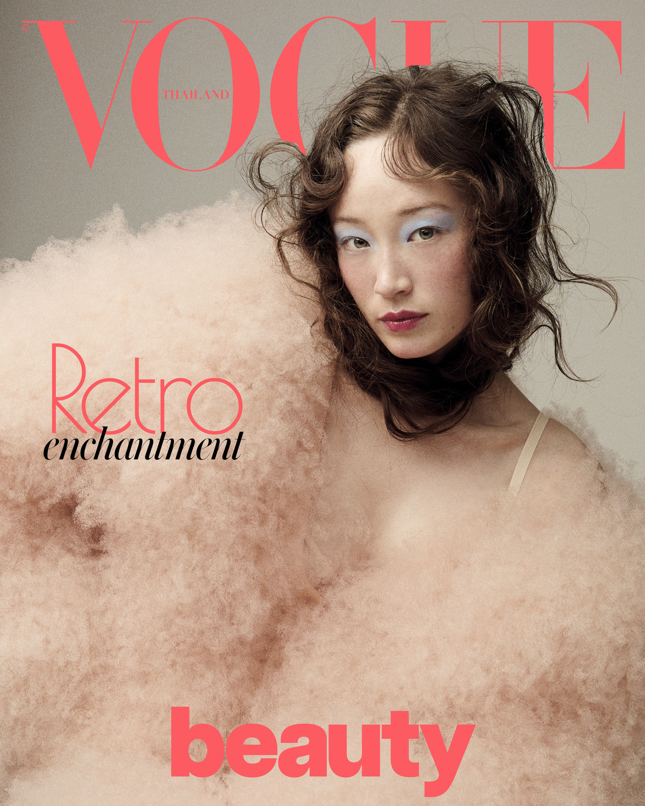 Vogue Thailand cover featuring a woman with blue eyeshadow and curly hair, posing in front of a pink logo and a fuzzy peach prop.