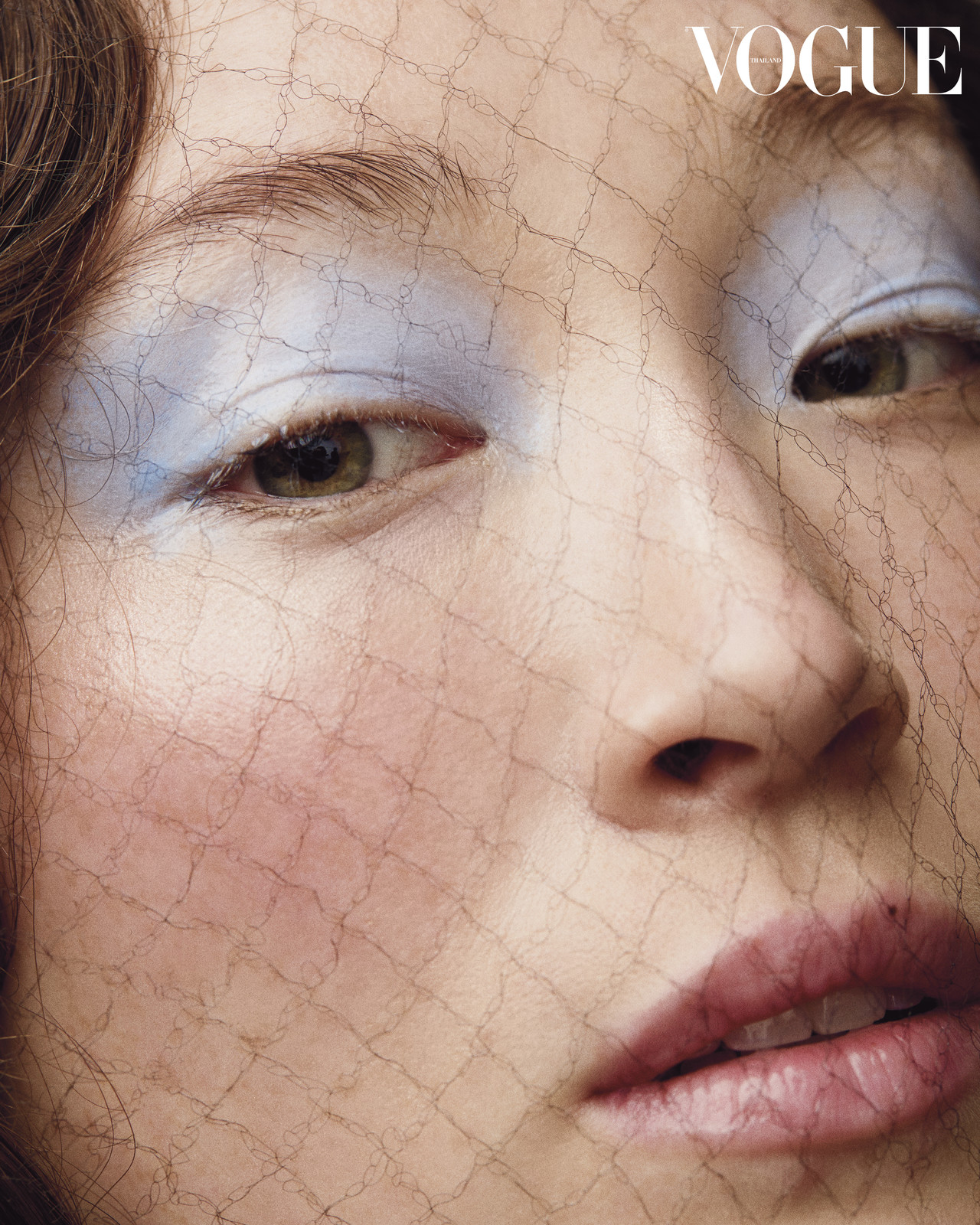 Close-up studio shot of a female face with light blue eyeshadow, pink lips, and a net veil, Vogue magazine logo is visible.