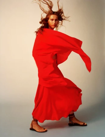 Model Angelina Kendall captured mid-motion wearing a voluminous red cape dress and strappy flat sandals in a studio setting.