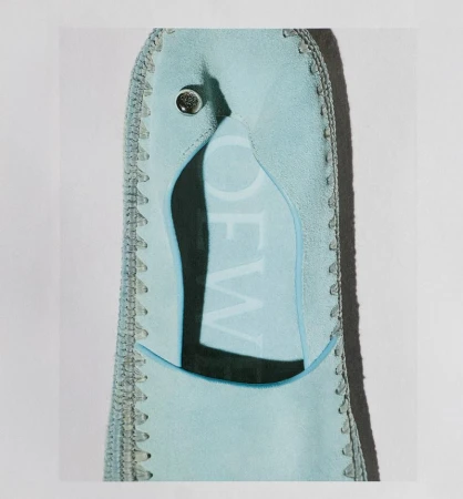 Close-up of light blue textile bag with button and stitched edges; includes the partial 'LOEW' brand name, showcased indoors on a white backdrop.