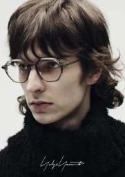 Close-up portrait of a model wearing translucent geometric eyeglasses and a black textured turtleneck sweater against a plain backdrop.