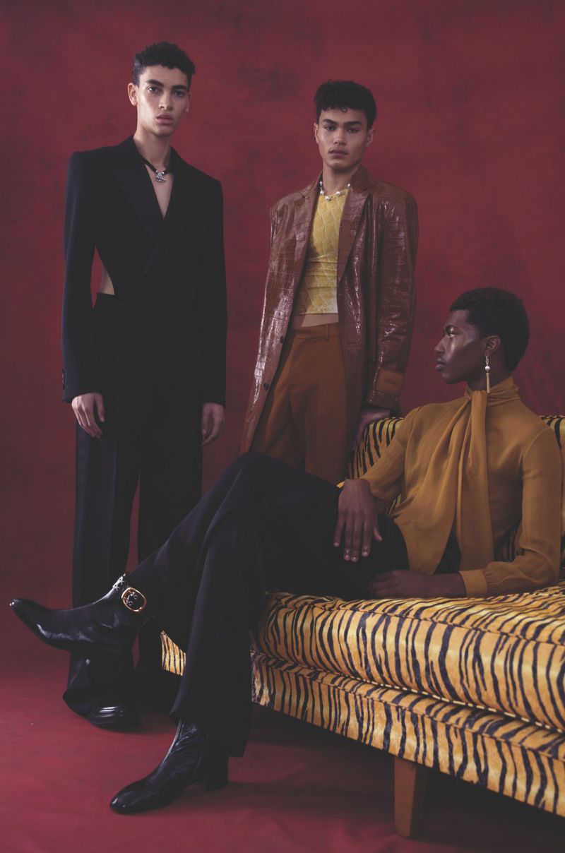 Three fashionable young adult models pose in coordinated outfits against a solid red backdrop, with one reclining on a tiger-striped chaise lounge.