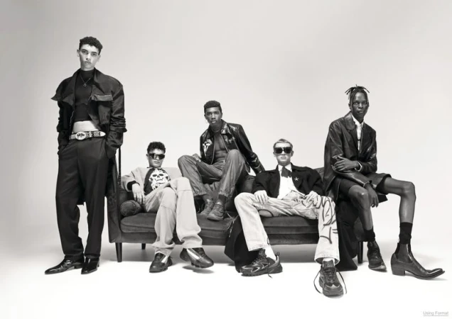 Monochrome fashion editorial featuring a group of five male models posing together on a dark couch against a white background.