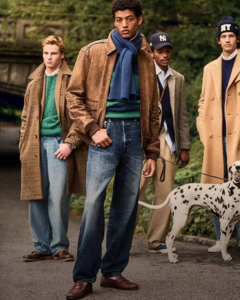 Four men pose on a path with a Dalmatian, wearing jackets, sweaters, jeans, and baseball caps in an outdoor setting with greenery.