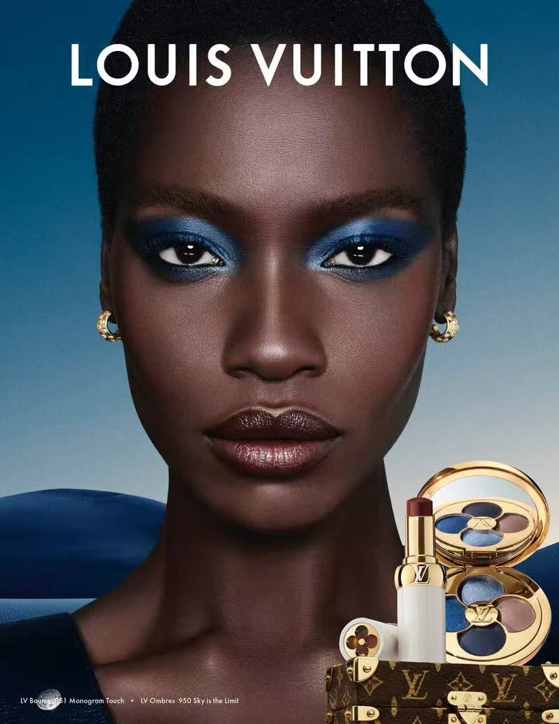 Close-up of a dark-skinned woman with blue eyeshadow posing in a beauty advertisement for Louis Vuitton cosmetics.