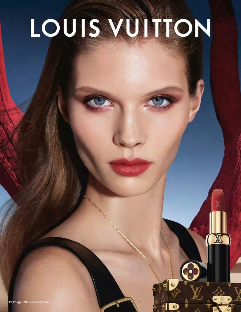 Cosmetic ad featuring a fair-skinned adult female model with red lipstick, eyeshadow, a gold necklace, and Louis Vuitton makeup and trunk.
