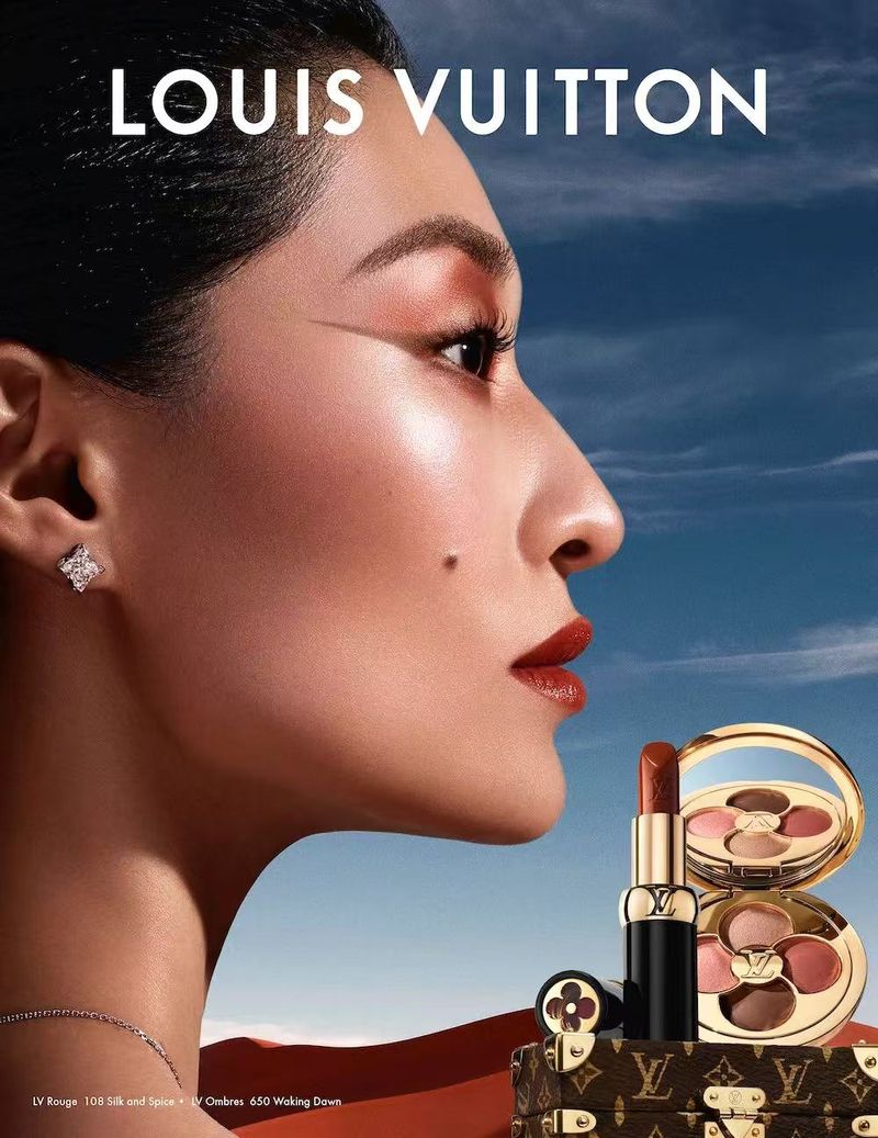 Cosmetics product shot featuring a woman in side profile wearing makeup and jewelry, set against a sky and desert backdrop.