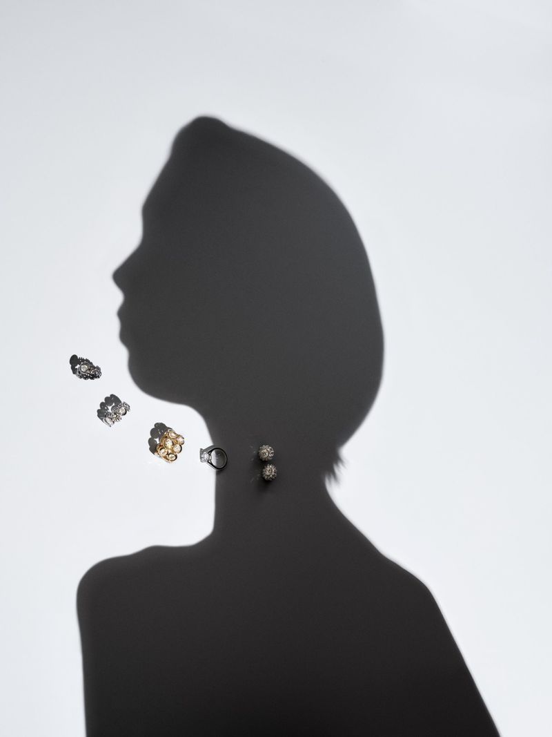 Striking studio shot features a woman's silhouette in profile, adorned with floating earrings and a ring, all set against a clean white backdrop.
