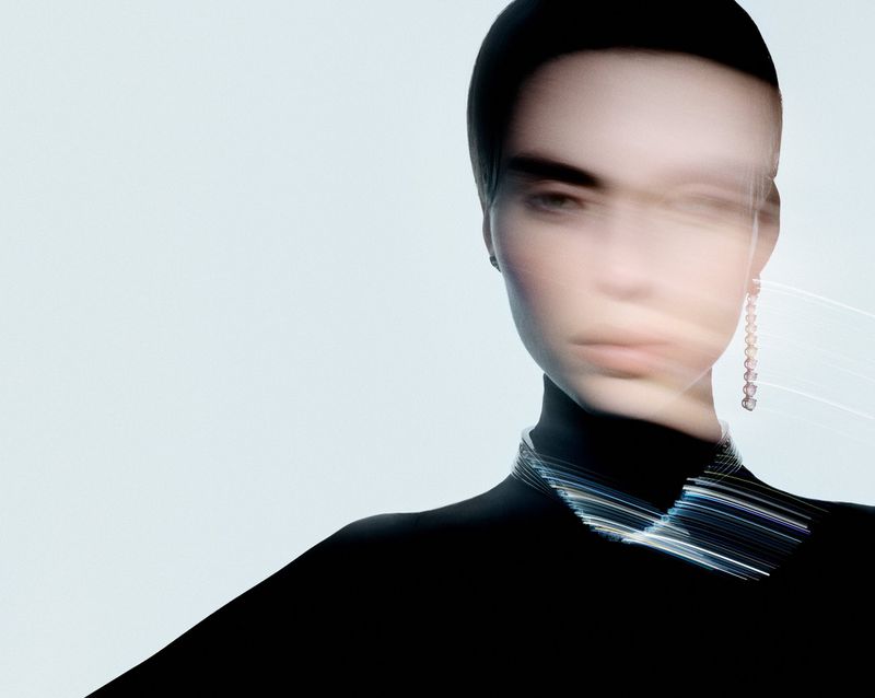 Fashion shot of a woman wearing a black top and silver choker with blurred motion effect in a studio setting against a light background.