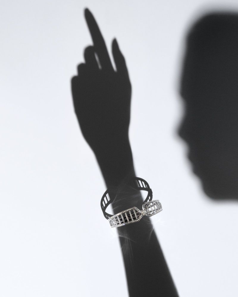Elegant studio shot of a woman's shadow wearing a modern silver bracelet with openwork design, against a simple white backdrop.