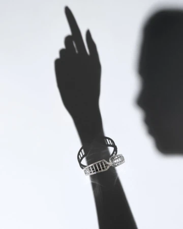 Elegant studio shot of a woman's shadow wearing a modern silver bracelet with openwork design, against a simple white backdrop.