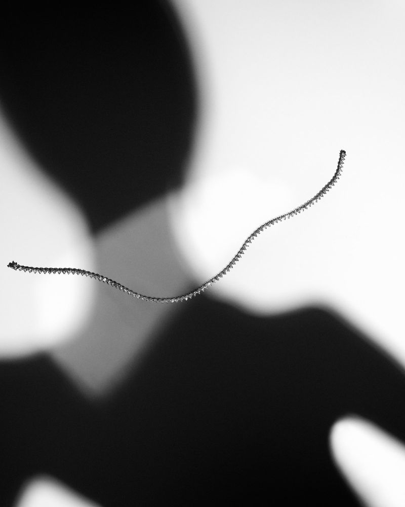 Monochrome photograph of a silver chain against a white background with a large, dark shadow suggesting the shape of a human figure.