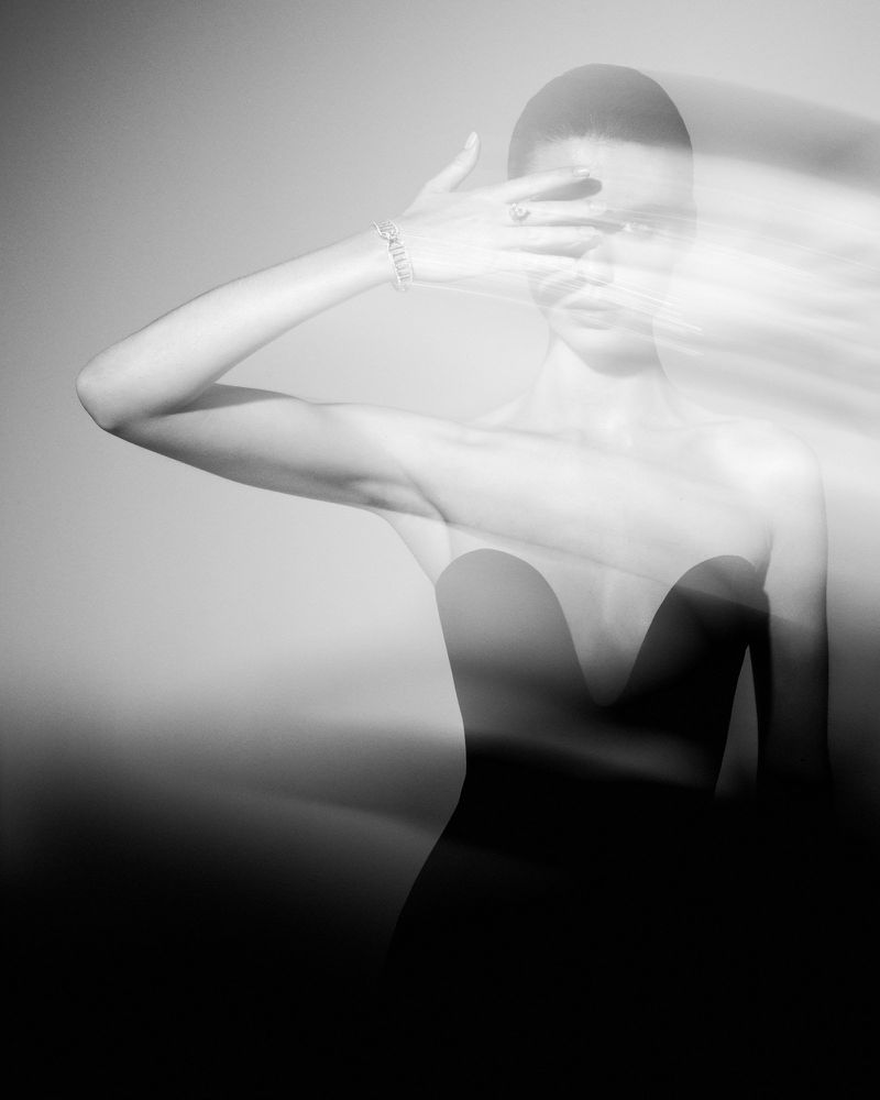 Monochrome portrait of a young woman with a blurred motion effect, covering her face with her hand, and wearing an elegant dress.