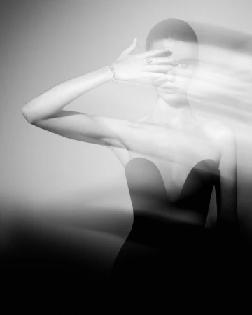 Monochrome portrait of a young woman with a blurred motion effect, covering her face with her hand, and wearing an elegant dress.