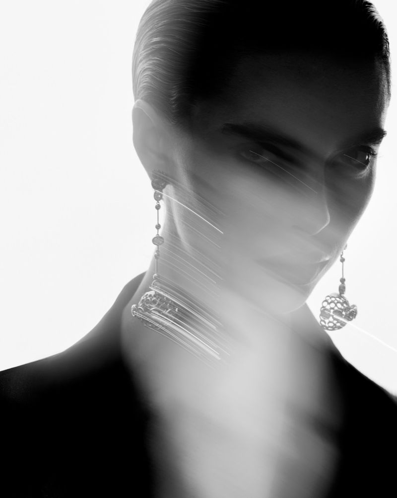 Monochrome portrait of a woman with slicked-back hair, wearing earrings and a jacket, in a high-key, seemingly motion-blurred photograph.