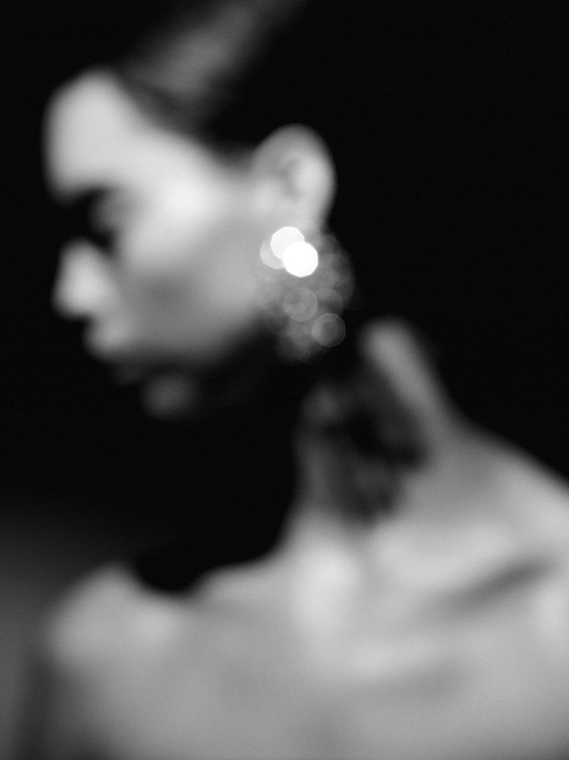 Monochrome portrait of a blurred woman with earrings and a dark background, capturing soft lighting and abstract qualities.