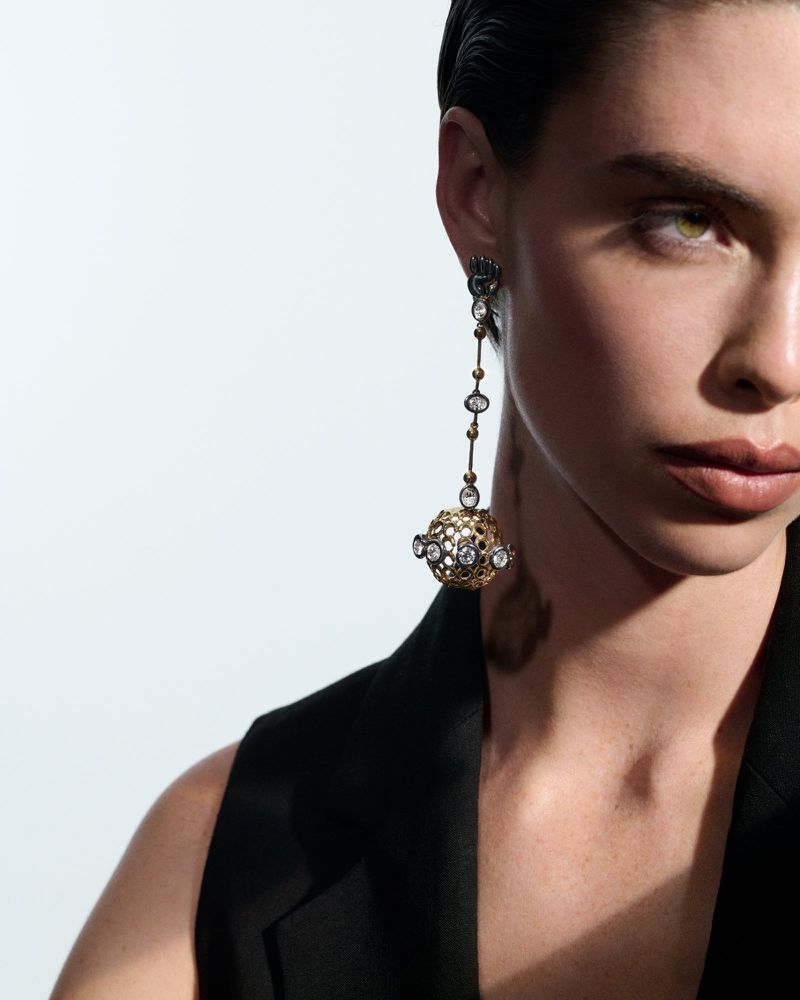 Elegant woman poses indoors with dangling decorative earrings. Close-up beauty shot against a white backdrop.