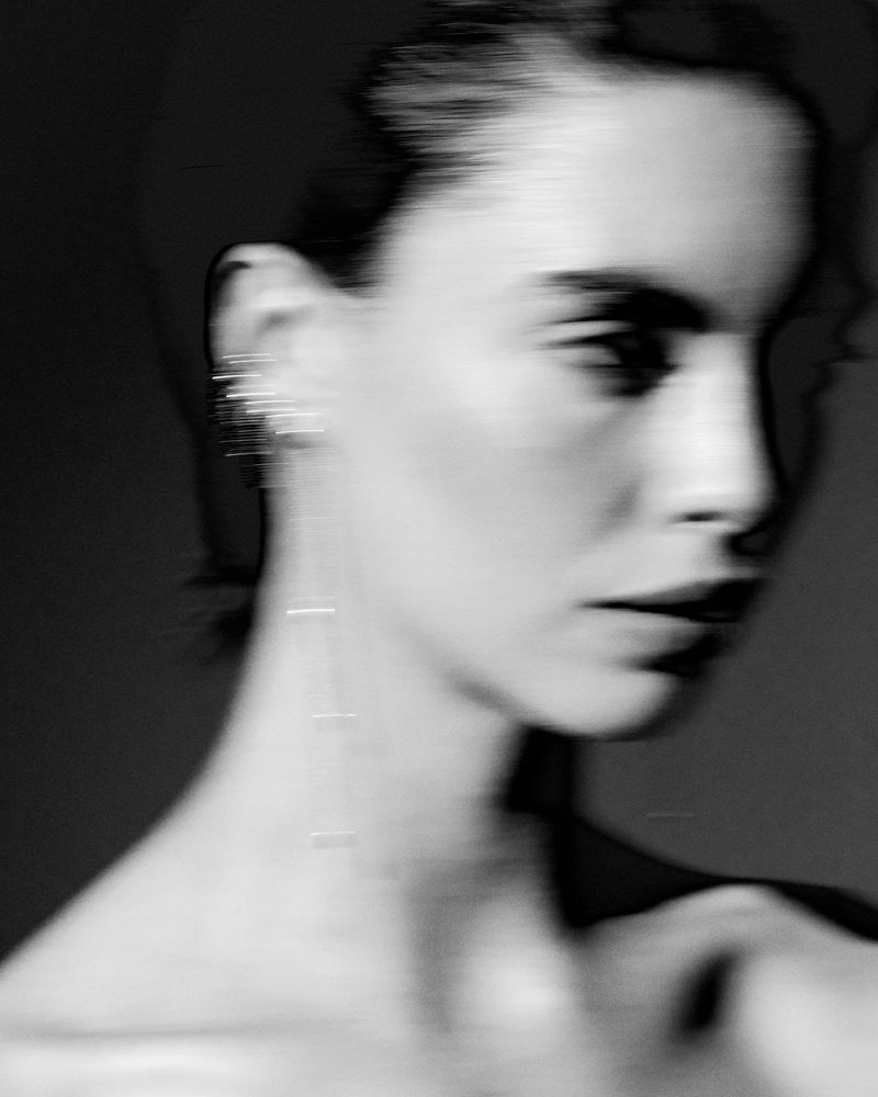 Monochrome portrait of a woman with blurred motion effects, wearing dangling earrings, and captured with shallow depth of field.