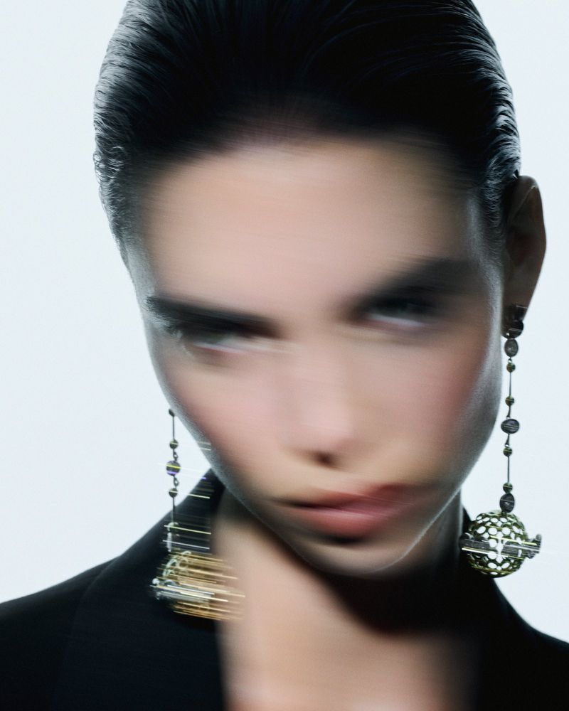 Close-up of a woman wearing dangling earrings and a black blazer against a white background in a studio setting.