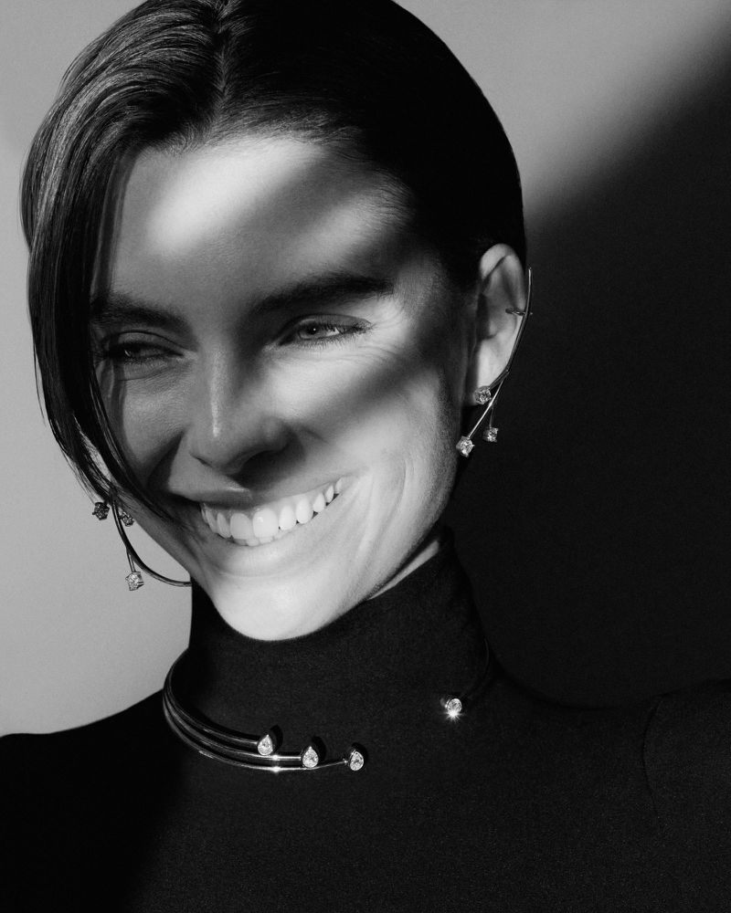 Smiling woman in a black turtleneck wearing a diamond-accented choker necklace and matching earrings in a black and white studio shot.