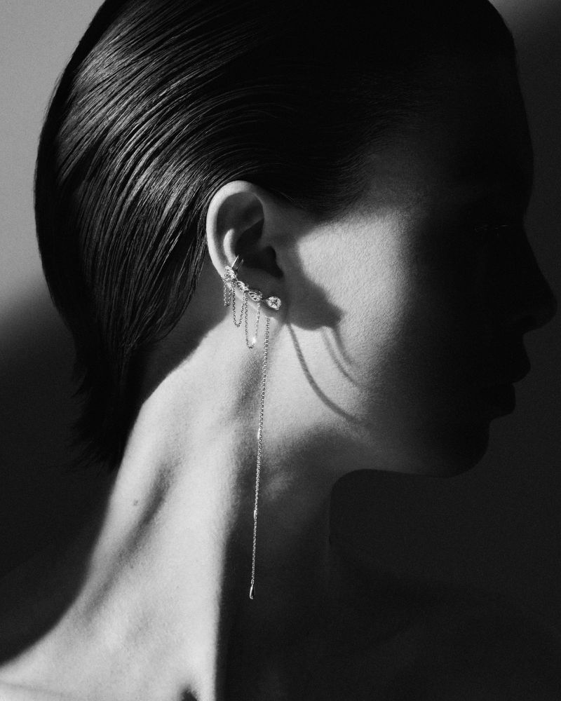 Close-up black and white portrait of a woman with wet hair and long, dangling jewel earring, against a shadowed backdrop.