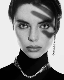 Black and white portrait of Candice Shepstone wearing a diamond necklace and earring with diagonal shadows across her face.