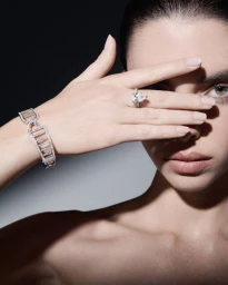 Close-up of model holding hand across face showcasing a diamond ring and bracelet against a dark background