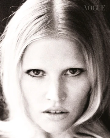 Black and white close-up portrait of model Lara Stone with winged eyeliner and blonde hair against a dark background.