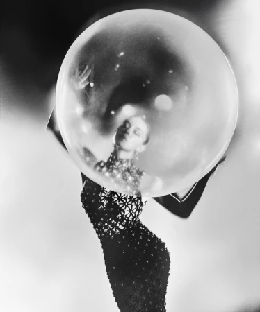 Monochrome fashion shot of a woman in a patterned gown, posing inside a large, transparent bubble against a gradient grayscale background.