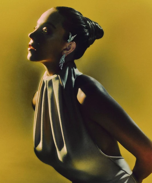 Woman in draped dress and earrings on yellow background. Fashion headshot with dark hair, looking up and away, minimalist and clean style.