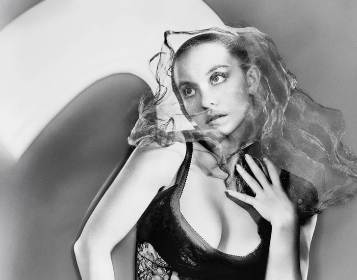 Portrait of Sydney Sweeney in black lingerie draped with a sheer veil against a curved studio backdrop