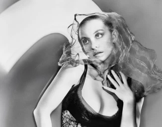 Portrait of Sydney Sweeney in black lingerie draped with a sheer veil against a curved studio backdrop