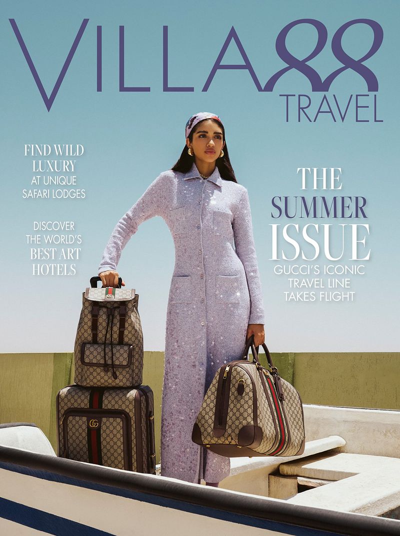 Magazine cover featuring a woman in a lavender dress, standing with luggage in a boat against a blue sky. Travel and fashion themes.
