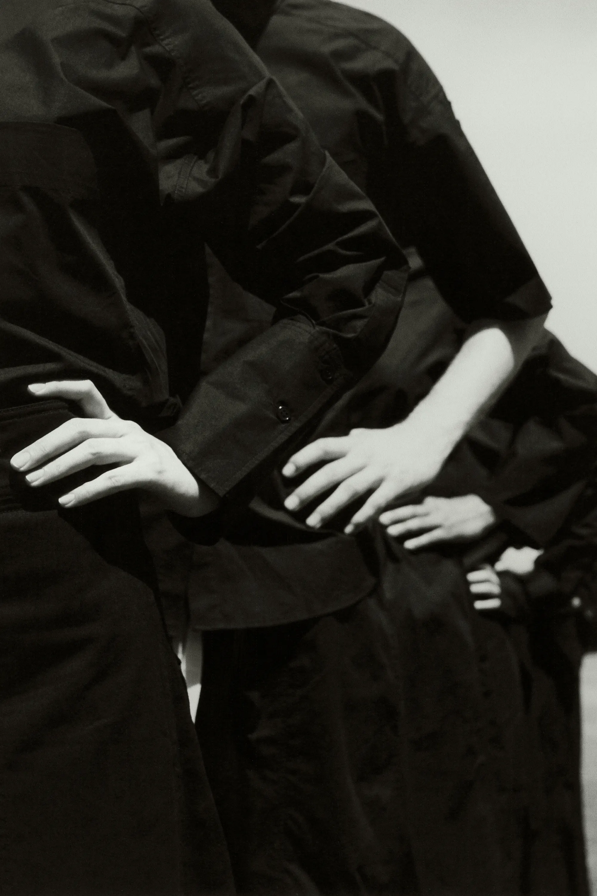 A monochromatic image showcases a row of people in dark shirts, with the focus on their arms crossed over their waists in a photo studio.