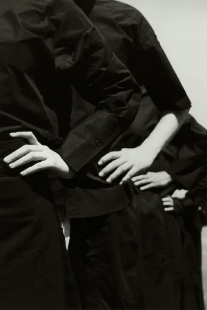 A monochromatic image showcases a row of people in dark shirts, with the focus on their arms crossed over their waists in a photo studio.
