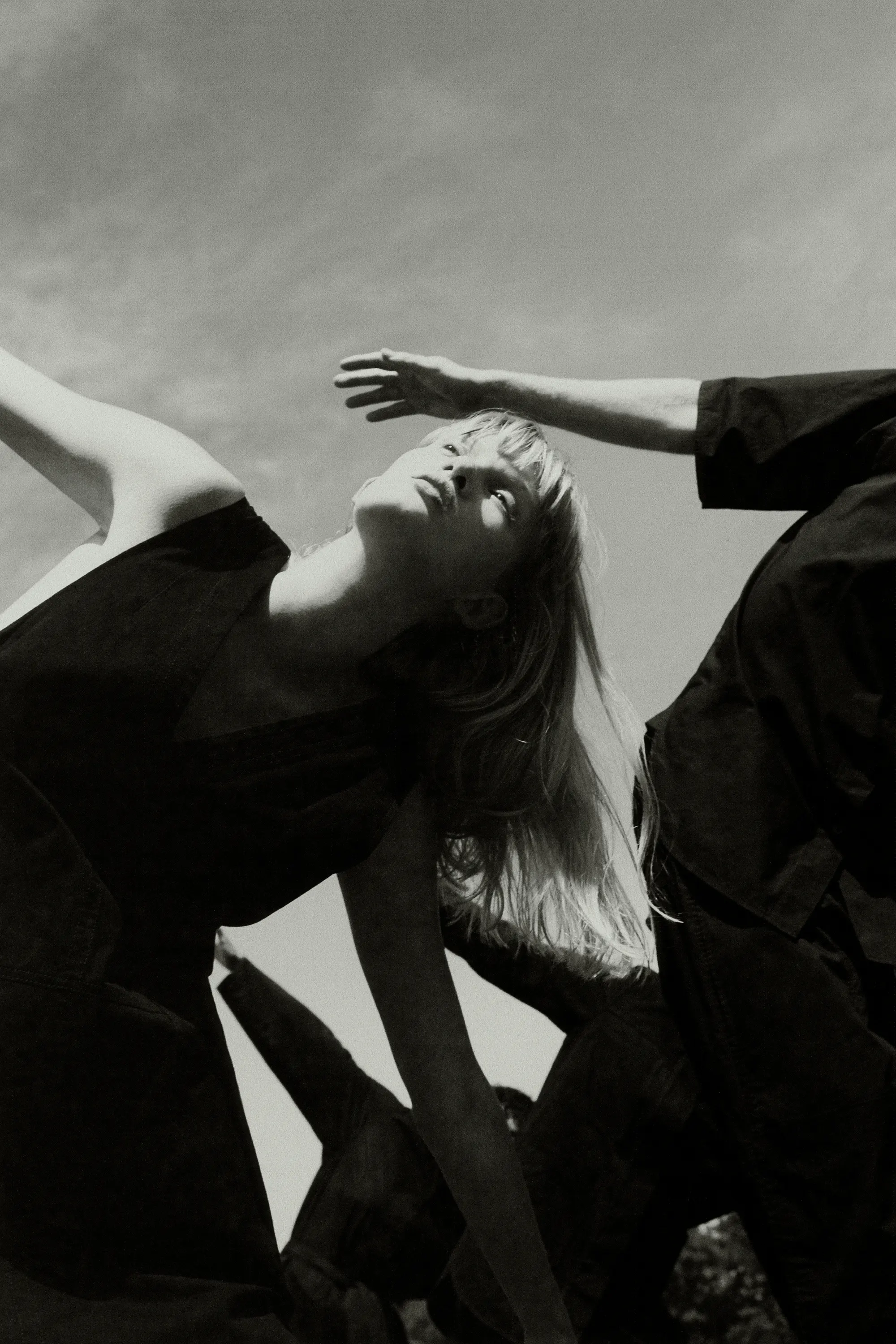 Monochrome portrait showcasing a woman with blonde hair, eyes closed, dressed in black, contrasted against a bright sky backdrop.