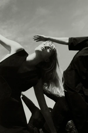 Monochrome portrait showcasing a woman with blonde hair, eyes closed, dressed in black, contrasted against a bright sky backdrop.