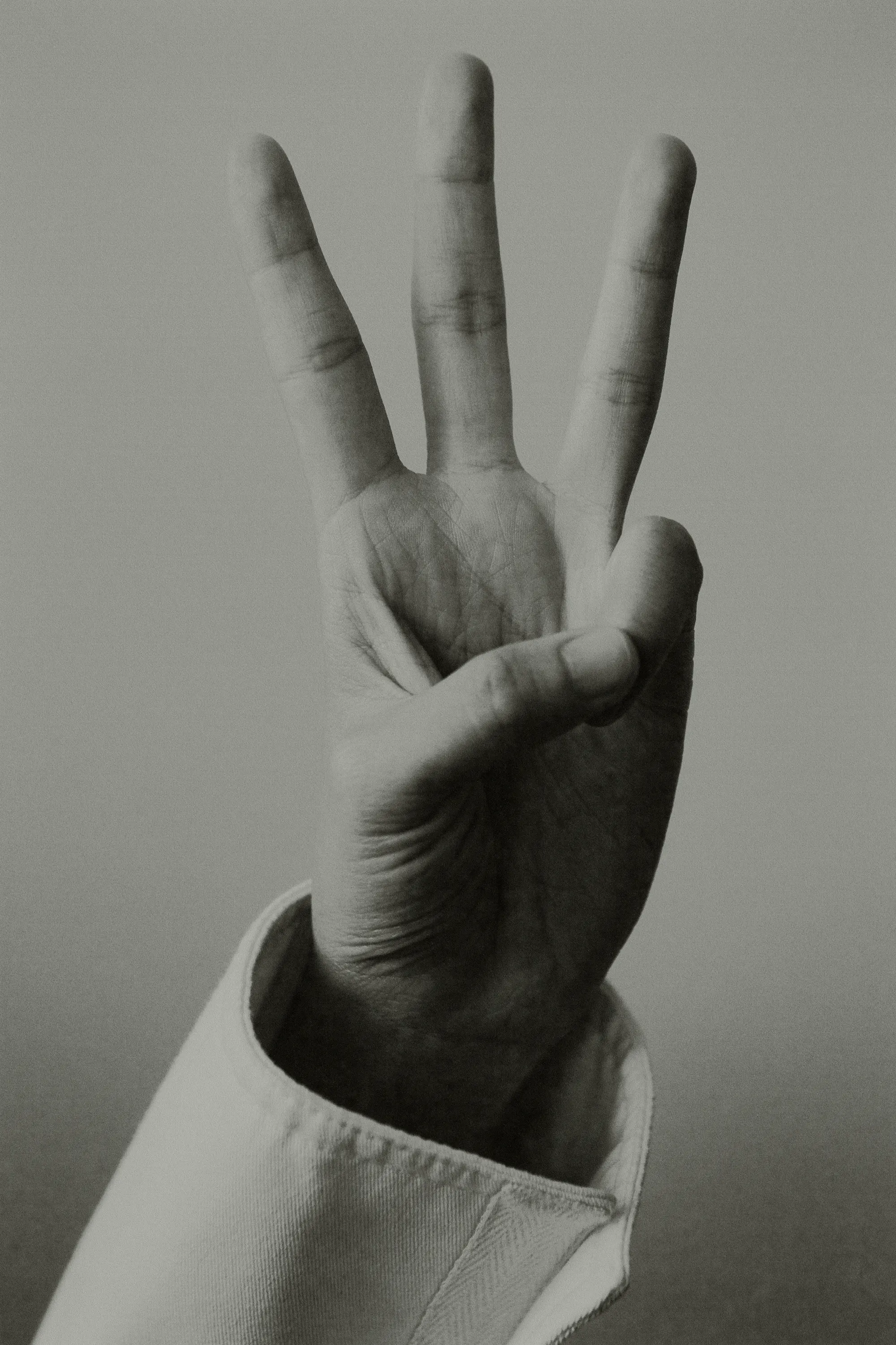 A close-up photograph features a hand held up displaying three fingers against a neutral backdrop, showcasing the gesture.