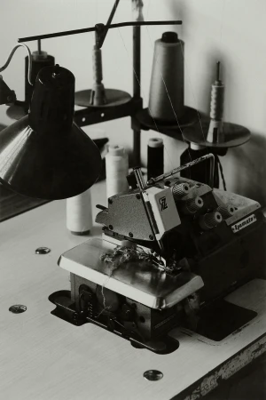Vintage sewing machine with cones of thread and a desk lamp in a workshop, captured in black and white with shallow depth of field.
