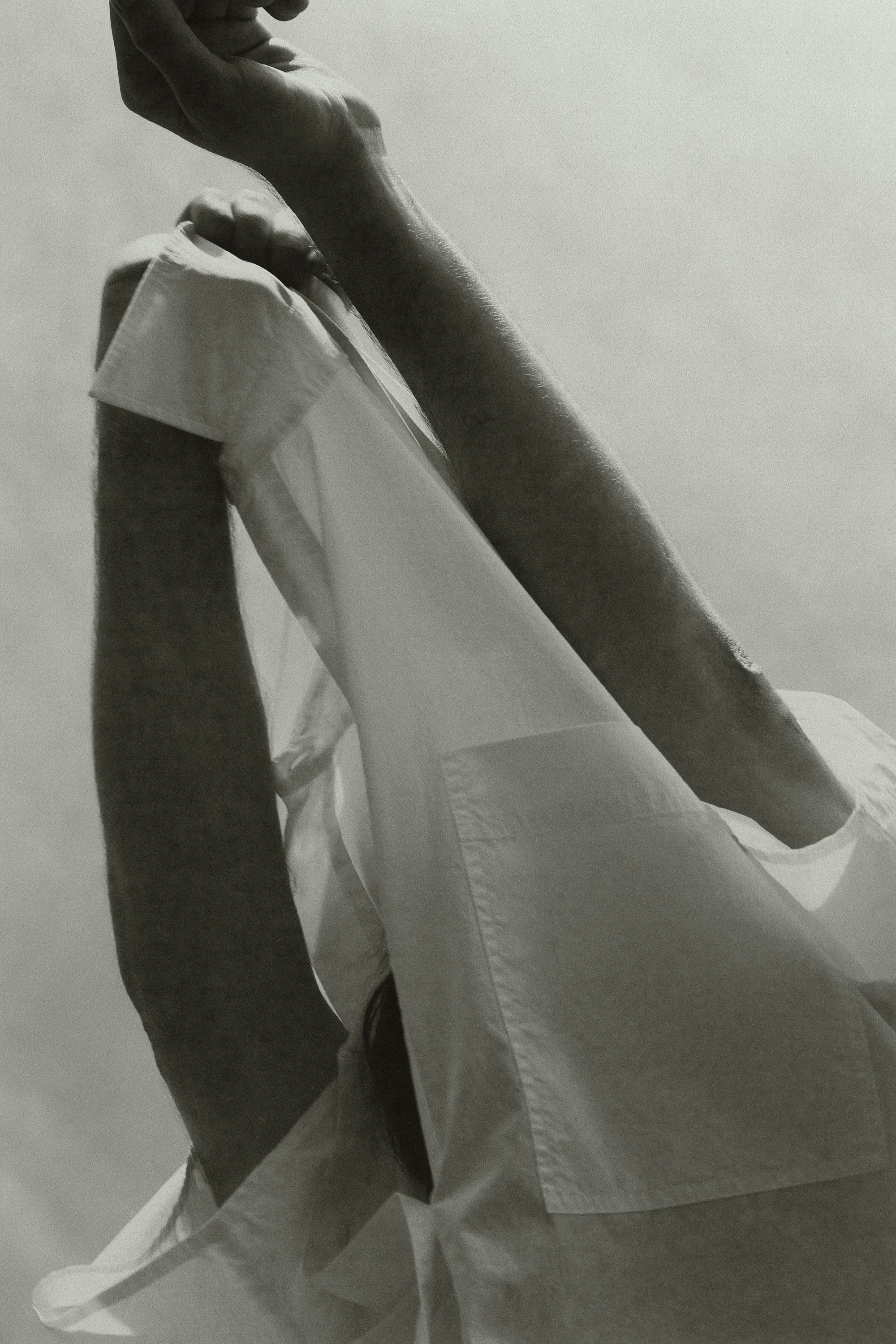 Monochrome close-up featuring a person in a white button-down shirt with arms raised against a bright sky background.