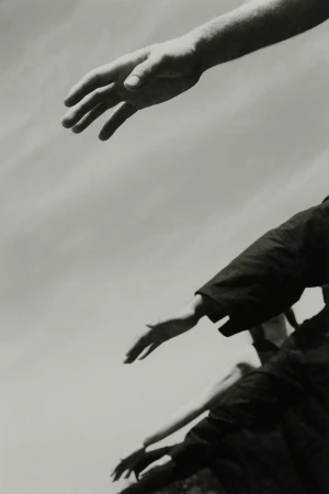 Black and white image features multiple arms and hands reaching upwards towards a bright, cloudy sky, creating a sense of ascent.
